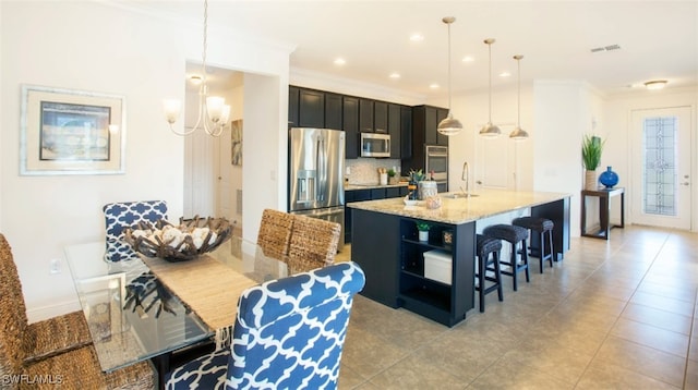 kitchen with pendant lighting, appliances with stainless steel finishes, sink, light stone counters, and a center island with sink