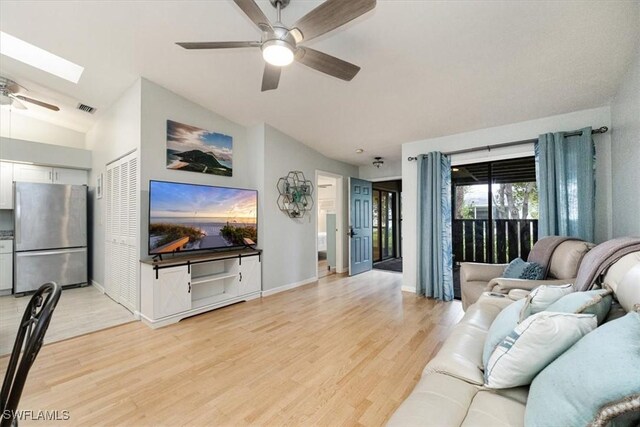 living room with light wood-type flooring, vaulted ceiling with skylight, and ceiling fan