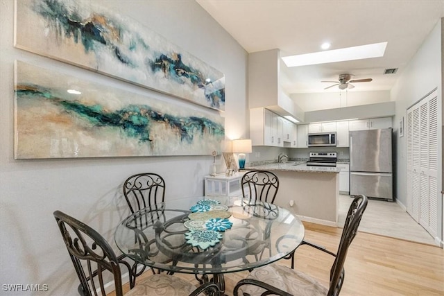 dining area with a skylight, visible vents, ceiling fan, light wood-type flooring, and baseboards