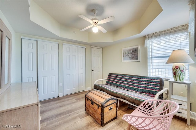 living area featuring ceiling fan, light wood-type flooring, and a tray ceiling