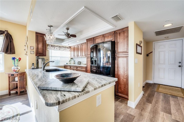 kitchen with black refrigerator, a tray ceiling, sink, kitchen peninsula, and light stone countertops