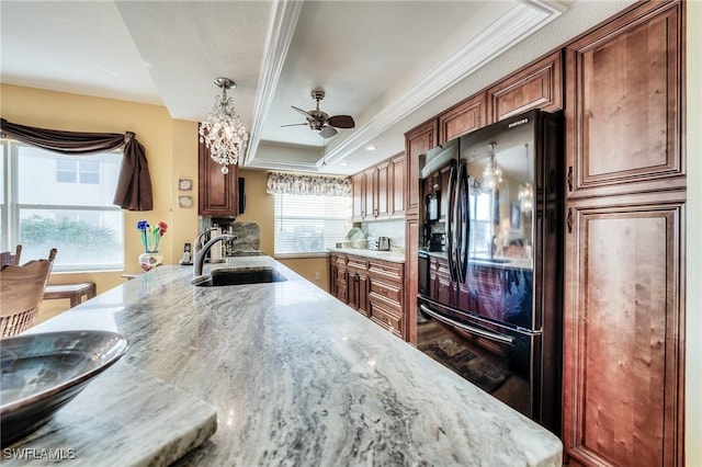 kitchen featuring sink, black refrigerator, ornamental molding, a tray ceiling, and light stone countertops