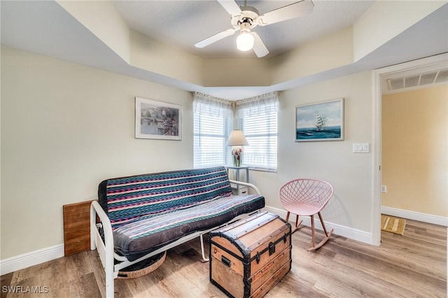 sitting room featuring ceiling fan, a raised ceiling, and light wood-type flooring