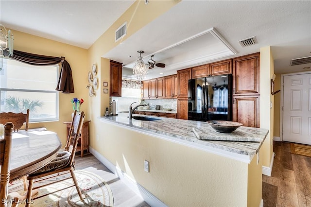 kitchen with sink, light stone countertops, black fridge, kitchen peninsula, and light wood-type flooring