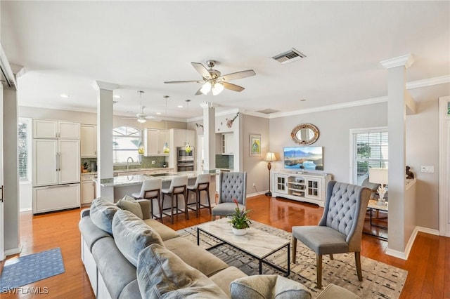 living room featuring ceiling fan, ornamental molding, decorative columns, and light hardwood / wood-style flooring