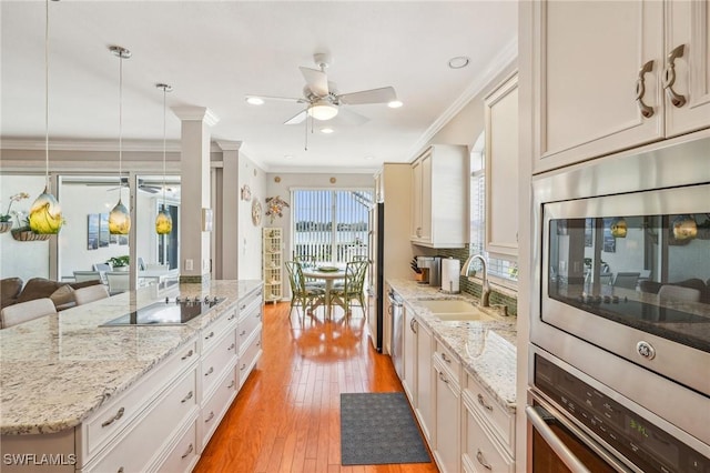 kitchen with sink, stainless steel appliances, light hardwood / wood-style floors, light stone countertops, and decorative light fixtures