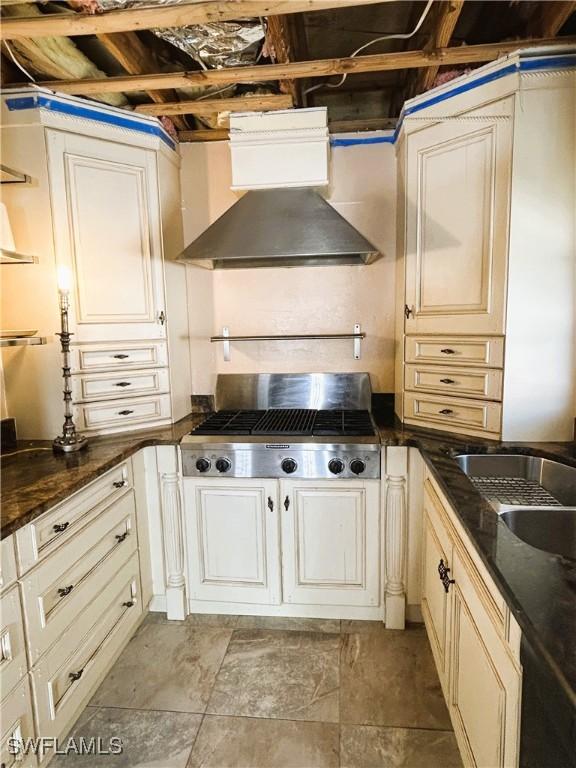 kitchen featuring stainless steel gas stovetop, sink, dark stone counters, and wall chimney range hood