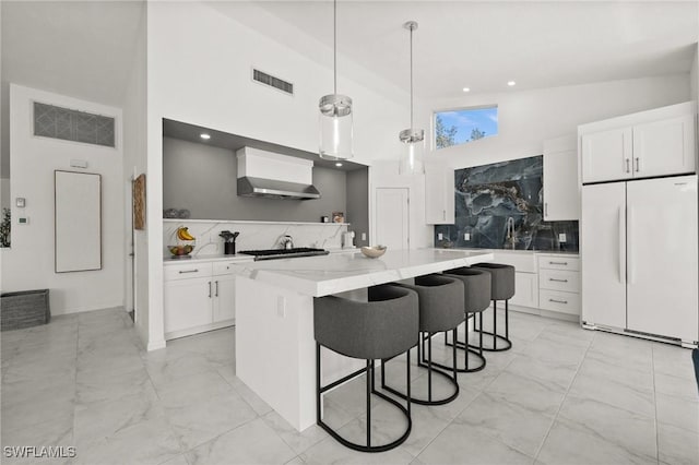 kitchen with white fridge, white cabinets, hanging light fixtures, and a center island