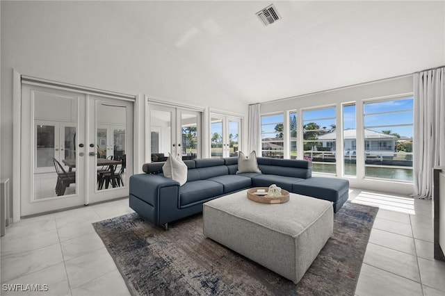 living room with a towering ceiling, light tile patterned flooring, a water view, and french doors