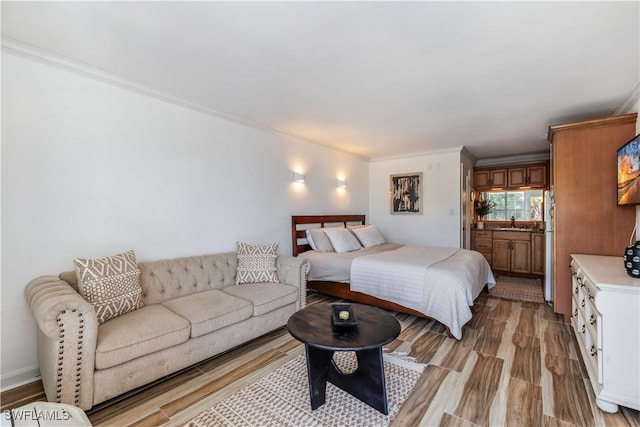 bedroom with freestanding refrigerator, light wood-type flooring, crown molding, and a sink