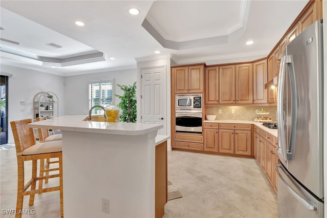 kitchen with a breakfast bar, a raised ceiling, tasteful backsplash, stainless steel appliances, and crown molding