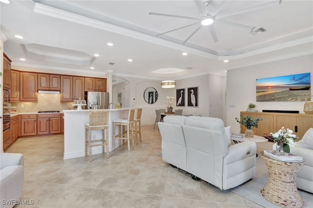 tiled living room with a tray ceiling, ornamental molding, and ceiling fan