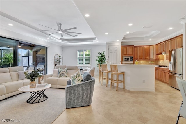 living room featuring light tile patterned flooring, ceiling fan, ornamental molding, and a tray ceiling