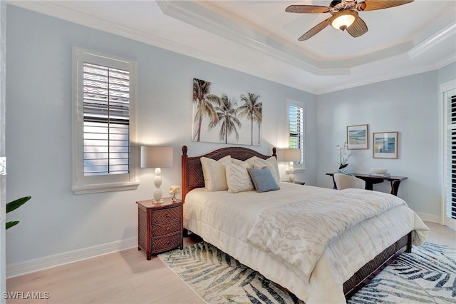 bedroom with ornamental molding, ceiling fan, light wood-type flooring, and a tray ceiling