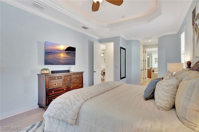 bedroom with crown molding, ensuite bath, a tray ceiling, ceiling fan, and light hardwood / wood-style floors