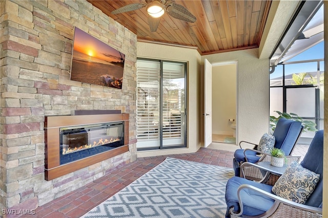 interior space featuring ceiling fan, wooden ceiling, and an outdoor stone fireplace