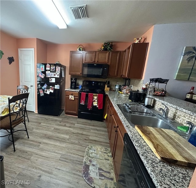 kitchen featuring tasteful backsplash, light wood-type flooring, stone counters, black appliances, and sink