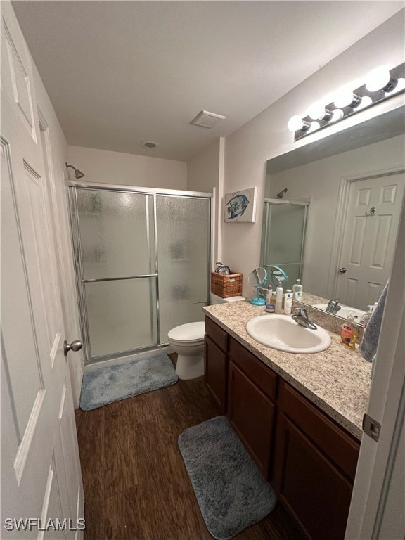 bathroom featuring a shower with shower door, vanity, wood-type flooring, and toilet