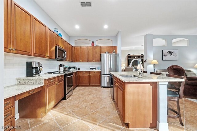 kitchen featuring a breakfast bar, sink, light tile patterned floors, appliances with stainless steel finishes, and decorative backsplash