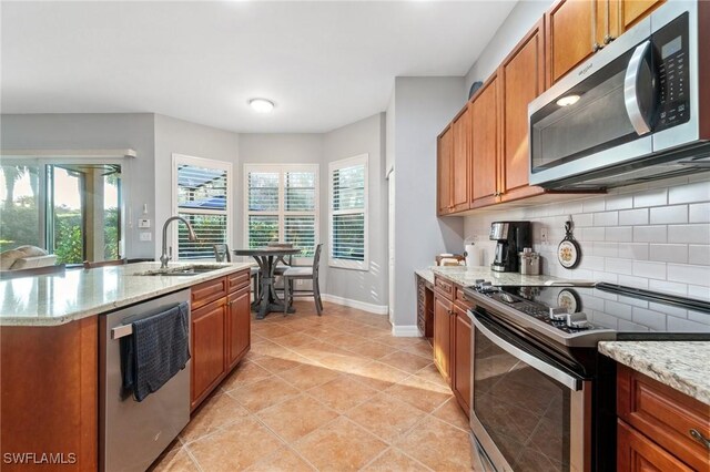 kitchen featuring appliances with stainless steel finishes, brown cabinetry, a sink, and decorative backsplash