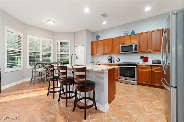 kitchen featuring a center island with sink, a breakfast bar area, visible vents, backsplash, and appliances with stainless steel finishes