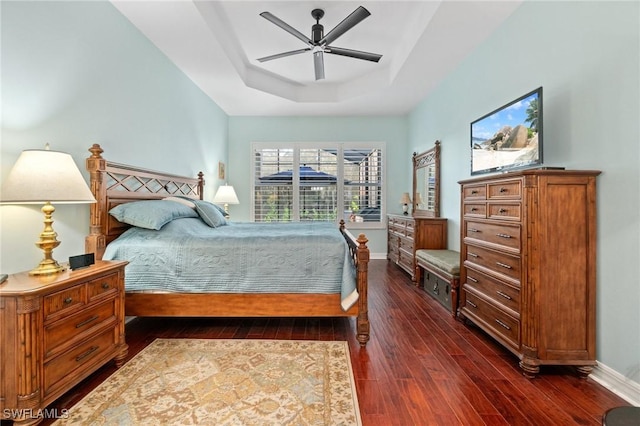 bedroom featuring a tray ceiling, dark wood finished floors, a ceiling fan, and baseboards