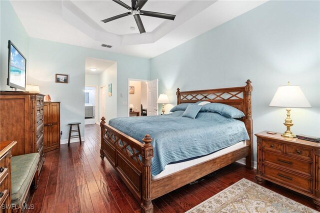 bedroom with ceiling fan, ensuite bath, dark hardwood / wood-style floors, and a raised ceiling