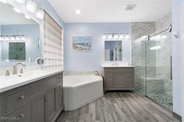 bathroom with visible vents, two vanities, wood finish floors, a shower stall, and a sink