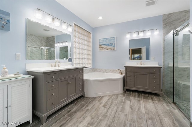 full bath with visible vents, two vanities, a sink, a shower stall, and a bath