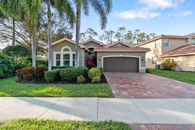 mediterranean / spanish home featuring a front yard, decorative driveway, an attached garage, and stucco siding