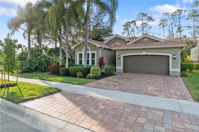 view of front of property featuring a garage, stucco siding, a tiled roof, decorative driveway, and a front yard