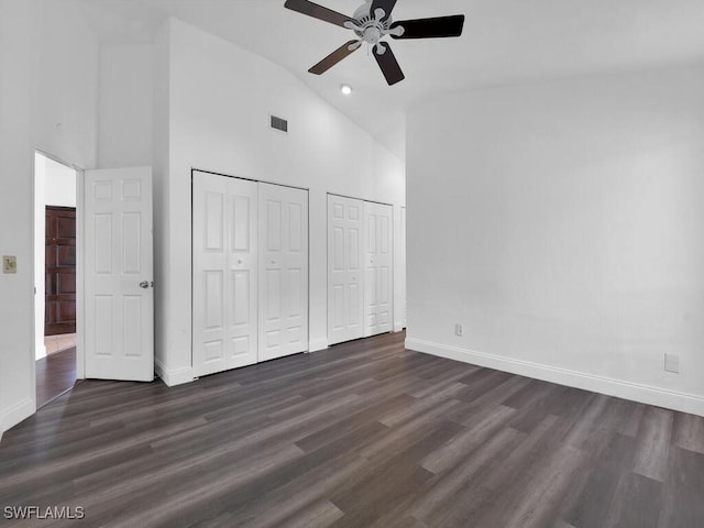 unfurnished bedroom featuring ceiling fan, dark wood-type flooring, high vaulted ceiling, and multiple closets