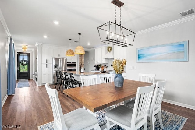 dining space featuring dark wood-type flooring, sink, crown molding, and a chandelier