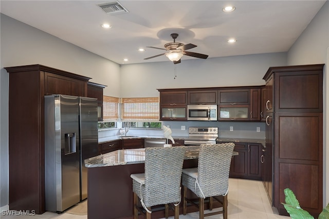 kitchen with light stone countertops, dark brown cabinetry, appliances with stainless steel finishes, a kitchen island, and light tile patterned floors