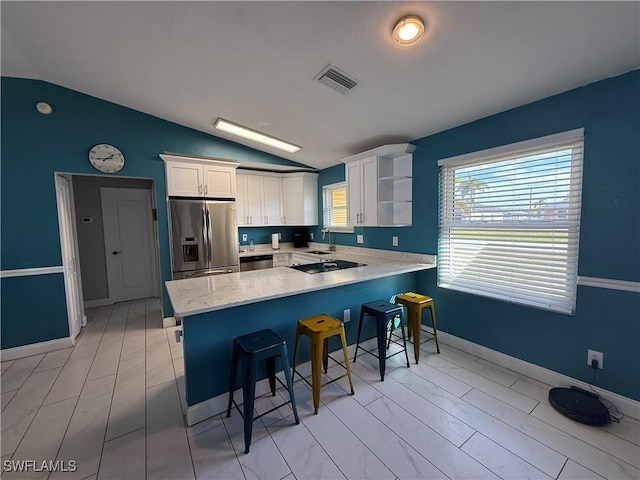 kitchen featuring white cabinetry, vaulted ceiling, appliances with stainless steel finishes, a kitchen breakfast bar, and kitchen peninsula