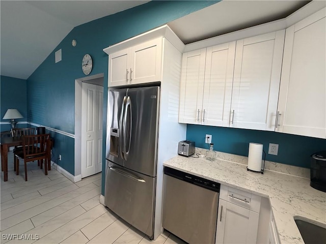 kitchen with light stone counters, appliances with stainless steel finishes, vaulted ceiling, and white cabinets