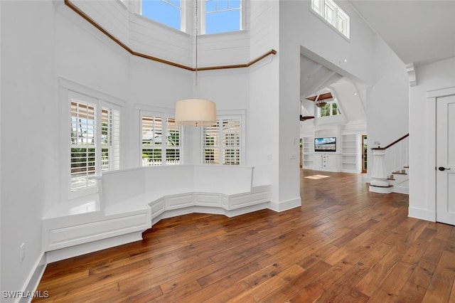 empty room with built in shelves, wood-type flooring, and a high ceiling