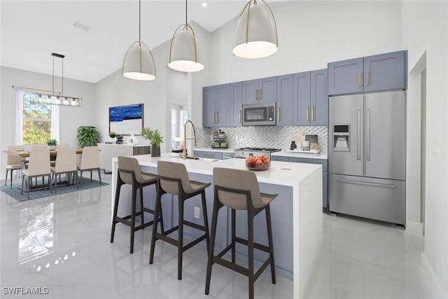 kitchen featuring a center island with sink, stainless steel appliances, tasteful backsplash, decorative light fixtures, and a breakfast bar