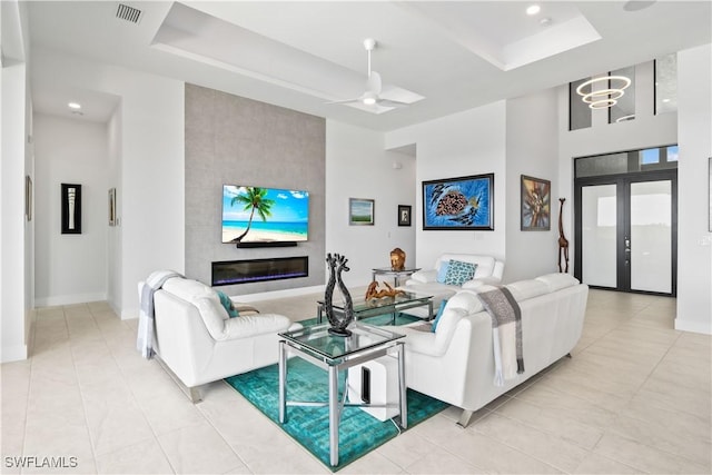 tiled living room with french doors, a large fireplace, a raised ceiling, and a towering ceiling