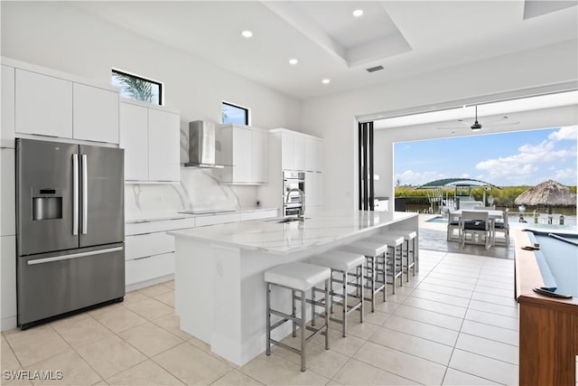 kitchen featuring white cabinetry, a kitchen bar, wall chimney range hood, stainless steel appliances, and a center island with sink