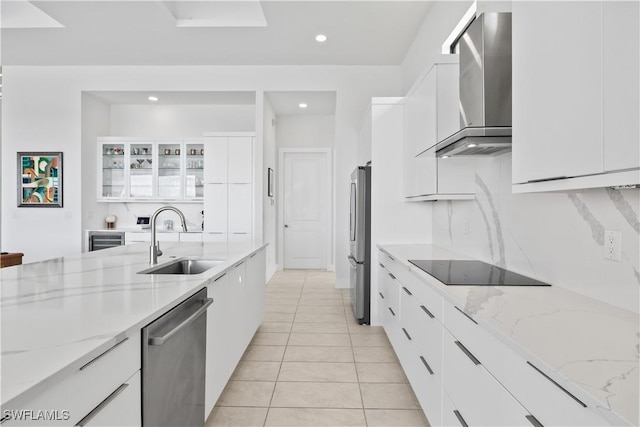 kitchen with light stone counters, appliances with stainless steel finishes, sink, and wall chimney range hood