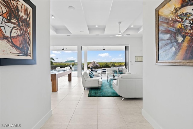 living room with plenty of natural light, light tile patterned floors, ceiling fan, and a tray ceiling