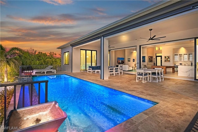 pool at dusk with ceiling fan and a patio