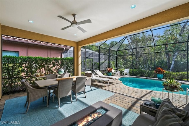 view of swimming pool featuring ceiling fan, glass enclosure, a fire pit, and a patio