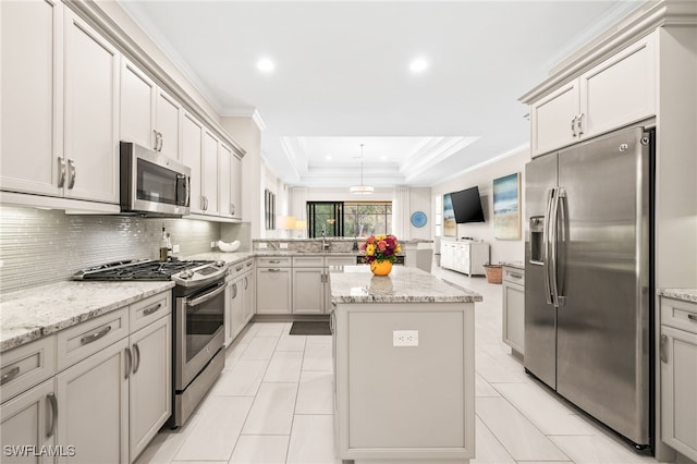 kitchen featuring appliances with stainless steel finishes, light stone counters, a tray ceiling, and a center island