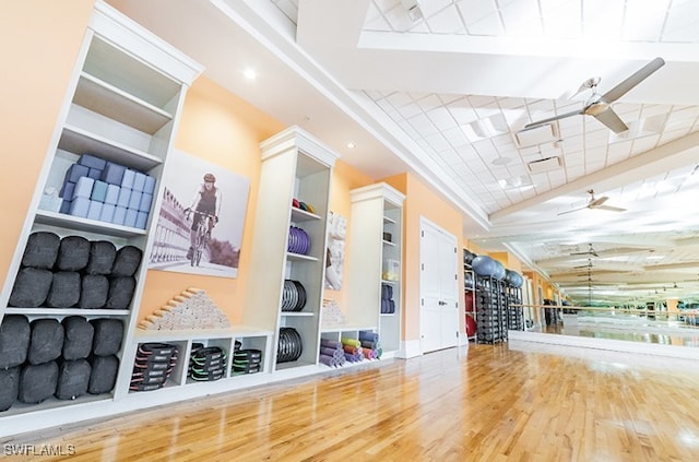 exercise area featuring hardwood / wood-style flooring, built in shelves, lofted ceiling, and ceiling fan