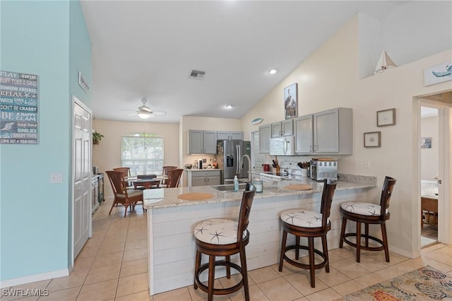 kitchen with light tile patterned floors, kitchen peninsula, gray cabinets, and a kitchen bar