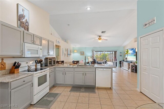 kitchen with light tile patterned floors, kitchen peninsula, white appliances, vaulted ceiling, and sink