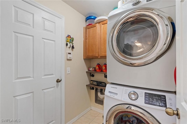 laundry area featuring stacked washer and dryer, light tile patterned flooring, and cabinets