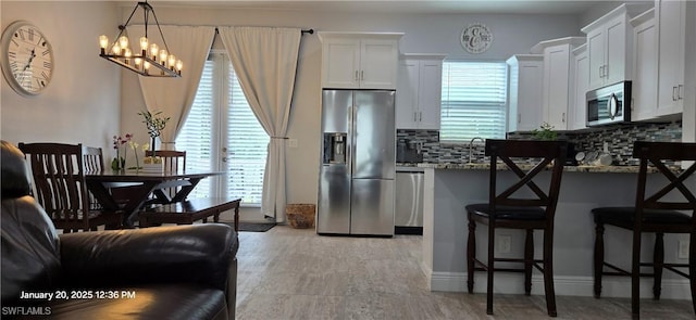 kitchen with appliances with stainless steel finishes, decorative backsplash, light stone countertops, white cabinets, and a breakfast bar